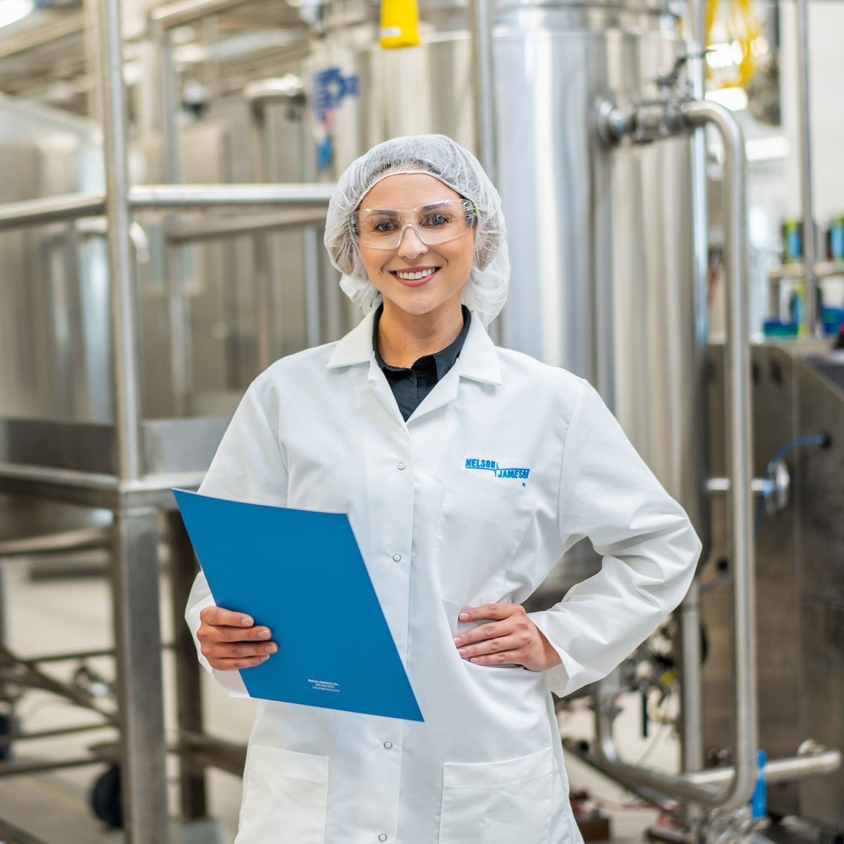 Start-Career_Jordyn-Warosh-standing-in-front-of-equipment-with-hand-on-hip-smiling-at-camera-holding-nj-folder